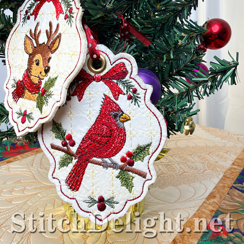 Close-up of the embroidered cardinal tag with a gold eyelet and red bow, with the matching deer tag partly visible behind it