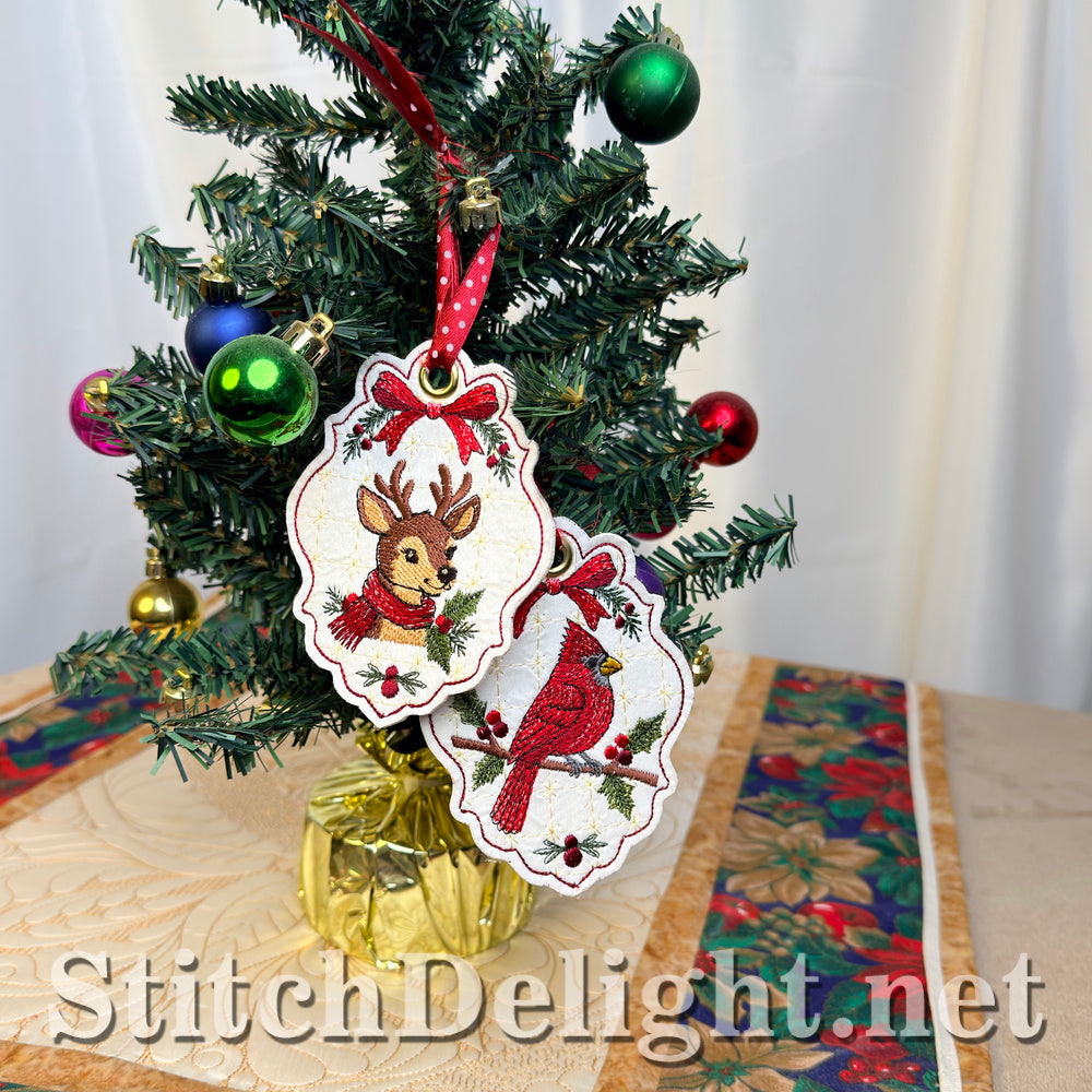 The cardinal and deer Christmas tags hanging together on a small decorated tree on a Christmas table runner