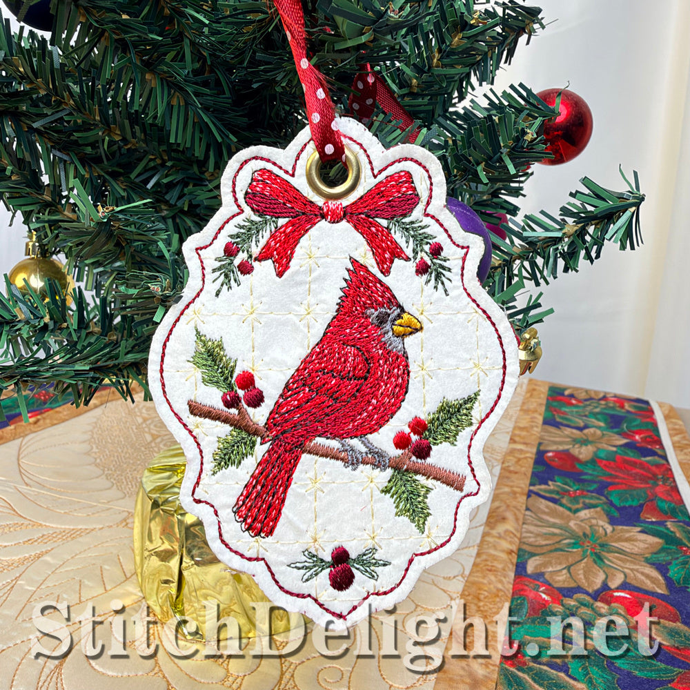 Cream vinyl Christmas tag embroidered with a red cardinal on a holly branch under a red bow, hanging from a red and white polka-dot ribbon on a small Christmas tree