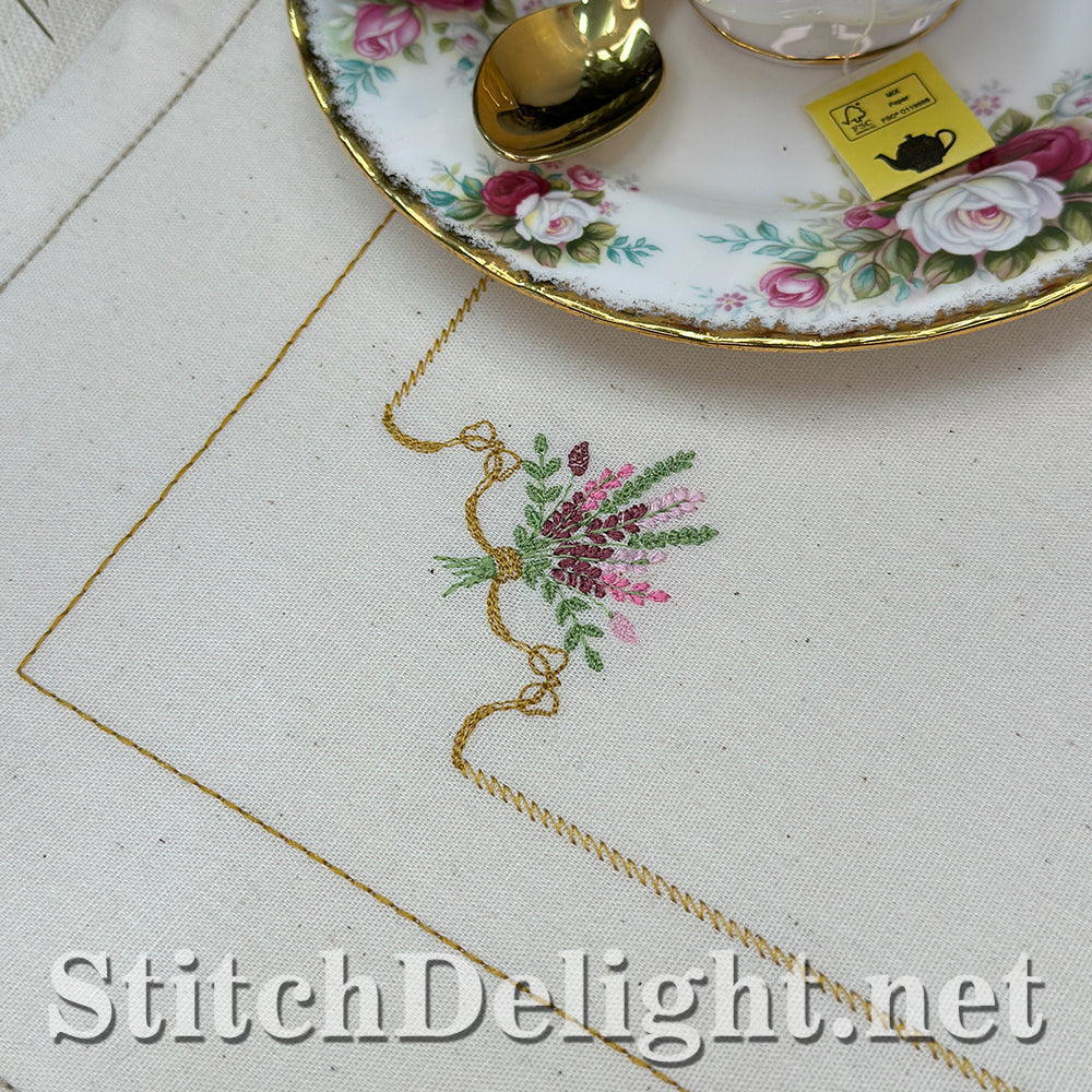 Embroidery work with floral design on fabric, next to a decorative teacup and saucer.