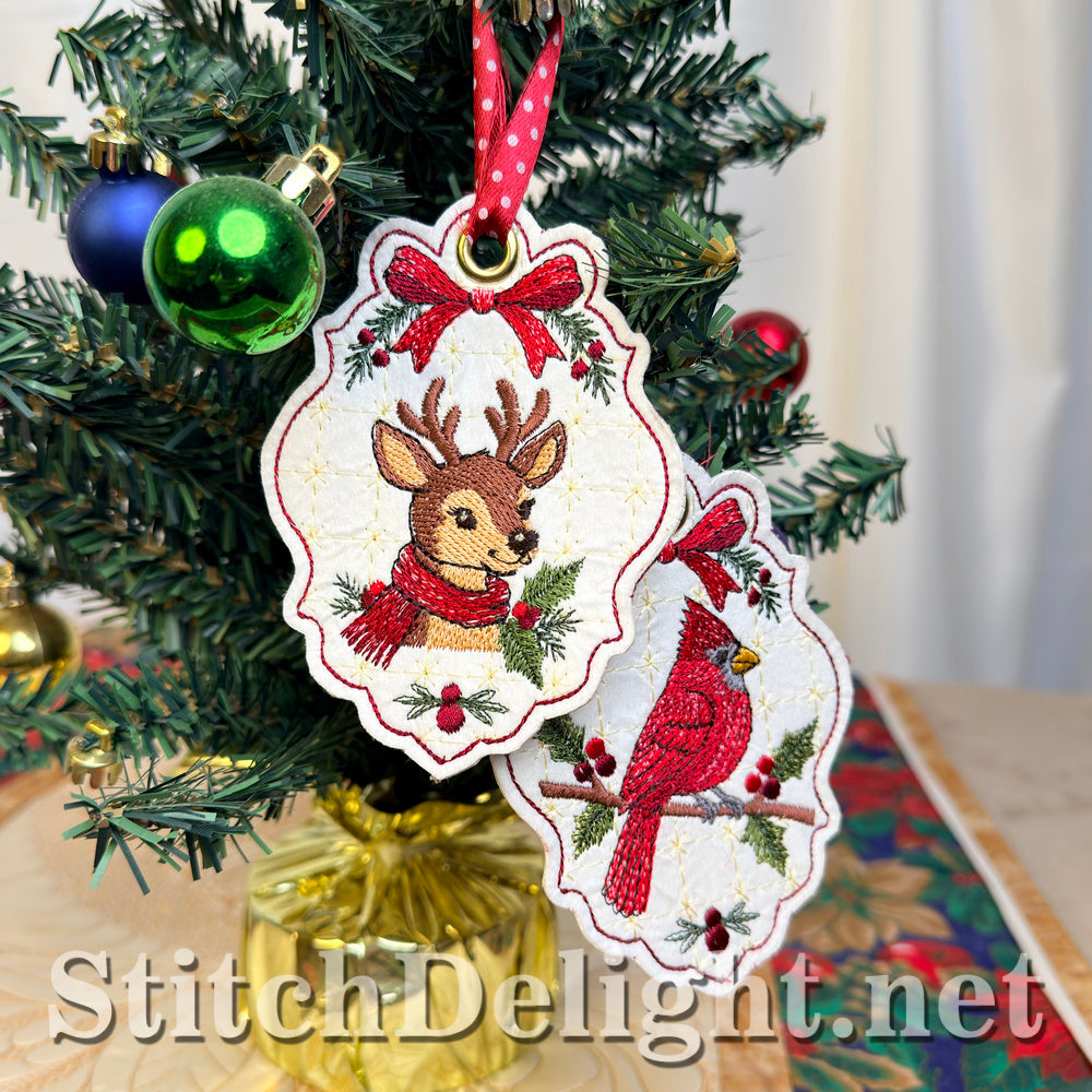 Embroidered deer tag in front of the matching cardinal tag, both hanging on a small Christmas tree