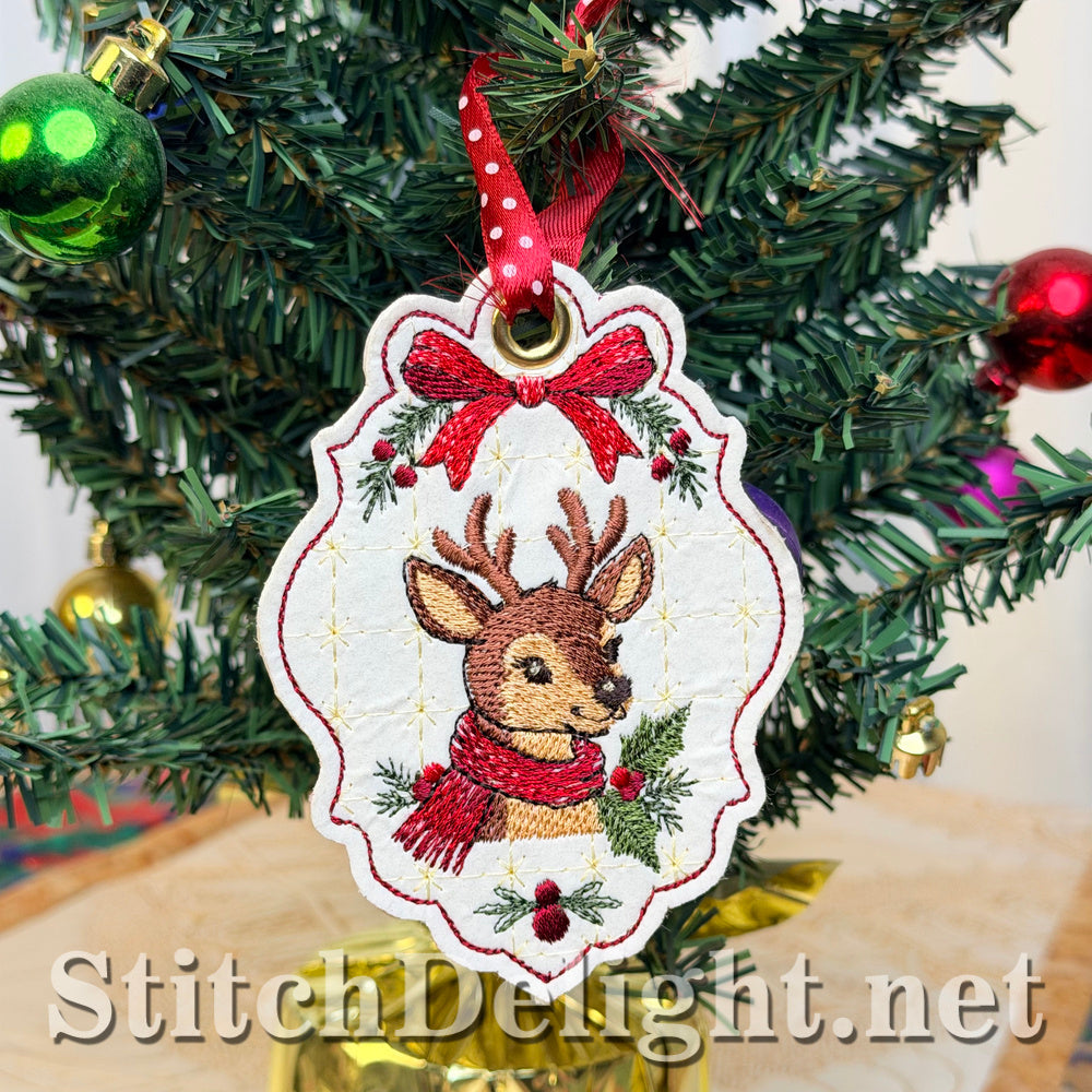 Cream vinyl Christmas tag embroidered with a deer in a red scarf under a red bow, hanging from a red and white polka-dot ribbon on a small Christmas tree