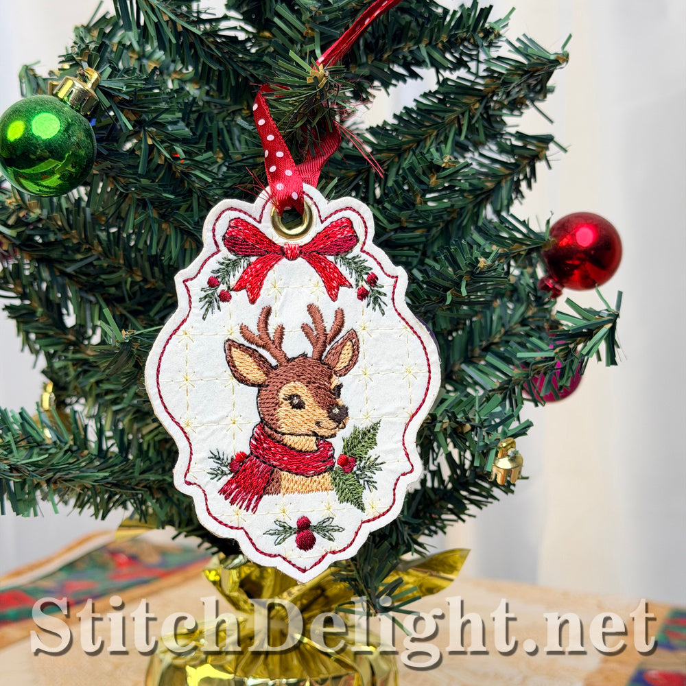 Embroidered deer tag in a red scarf hanging from a red ribbon on a miniature Christmas tree with red and green baubles